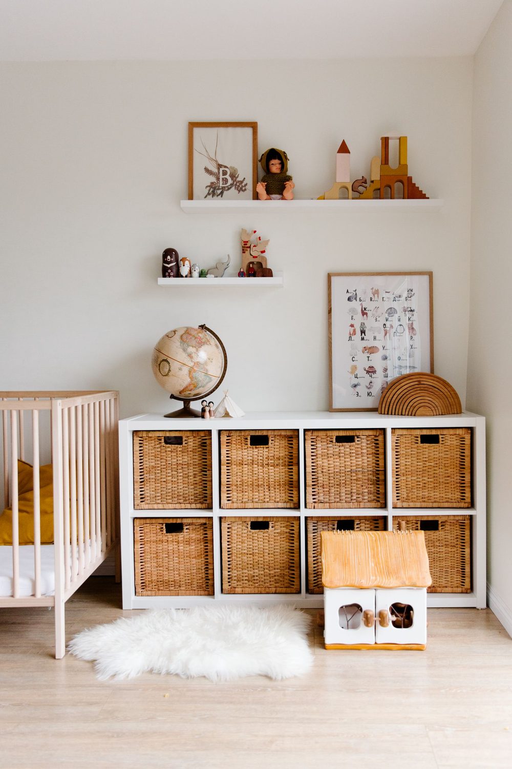 A children's room with a cot, woven storage baskets and a shelf of toys and a globe