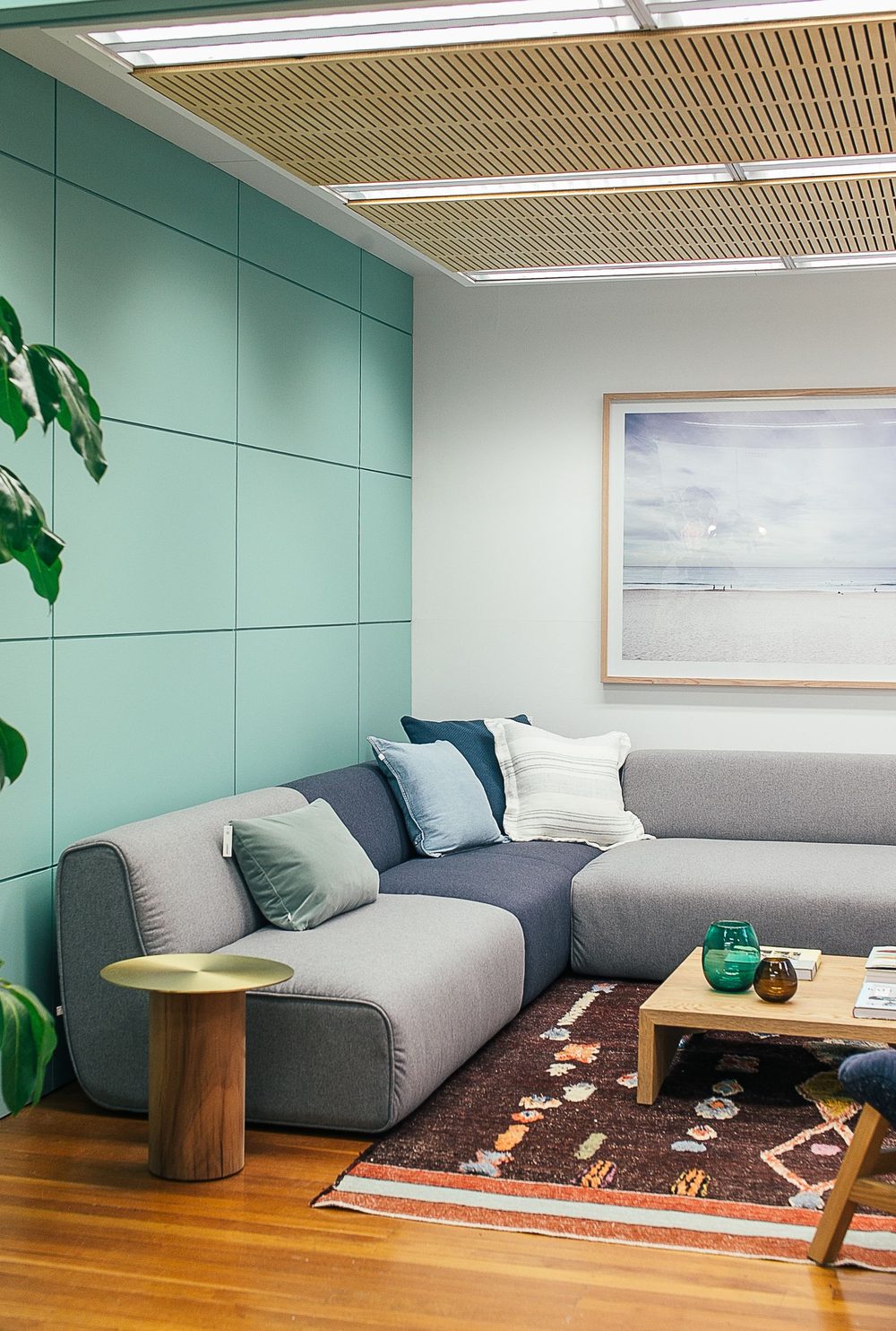 A living room with a grey corner sofa, teal panelling and warm wooden floor